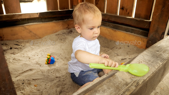 Little boy playing in sandpit with plastic toys and digging sand