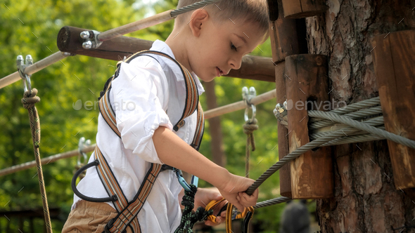 Little boy clamping safety rope hooks to the tree while climbing in rope  adventure park Stock Photo by kryzhov