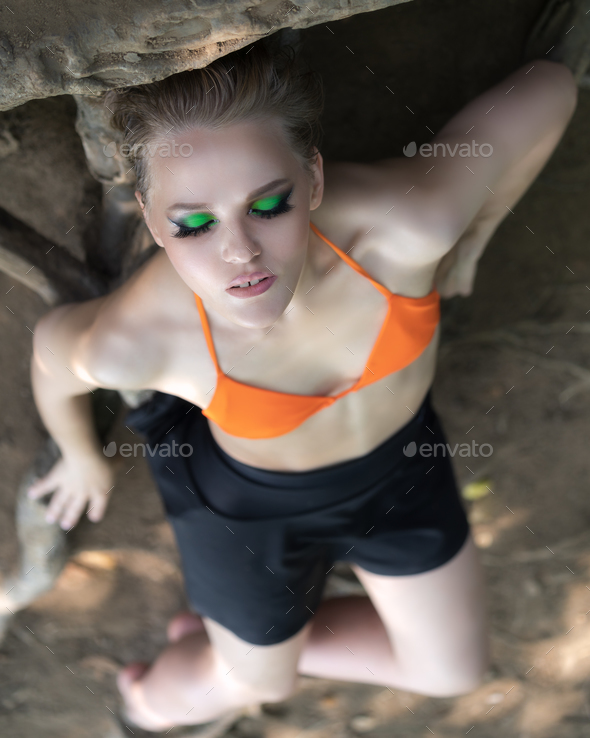 High angle shot blonde woman with eyes closed, bright make-up relaxation on ground on roots of trees