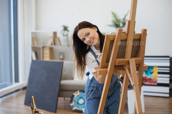 Fine artist peering out of frame on easel in modern studio