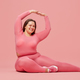 Smiling young plus size woman in sportswear stretching over pink background - PhotoDune Item for Sale