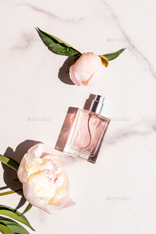 A chic bottle of feminine perfume or cosmetic spray on a marble background with a beautiful peony