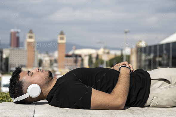 Relaxed young man lying in a balcony while listening music with headphones. Confident young guy