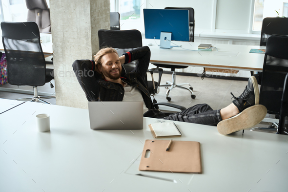 Satisfied guy comfortably settled down in coworking space with laptop
