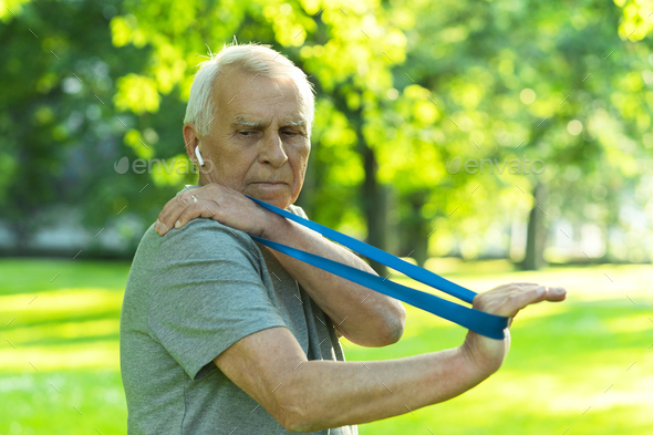 Active elderly man exercising with a rubber resistance band in green city park