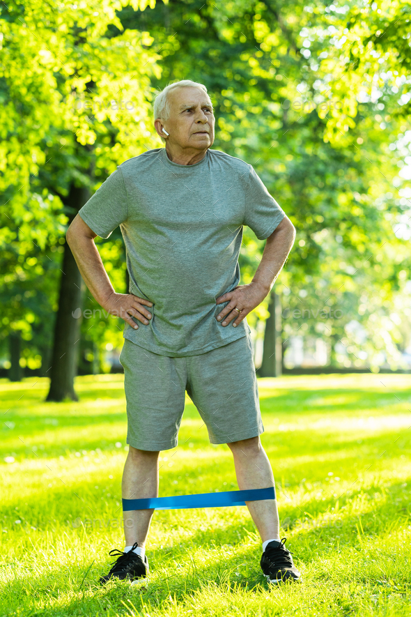 Active elderly man exercising with a rubber resistance band in green city park