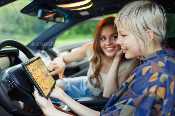 Happy two women driver tourist travelers with digital tablet USA American map at rental car vehicle.