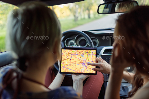 Happy young two women driver tourist with digital tablet USA American map at rental car vehicle.