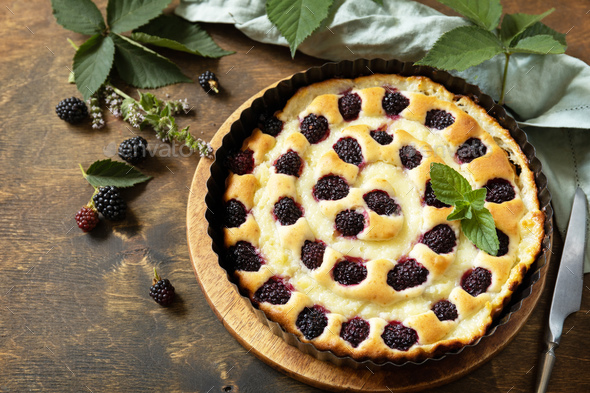 Sweet pie with blackberry and custard on wooden table.
