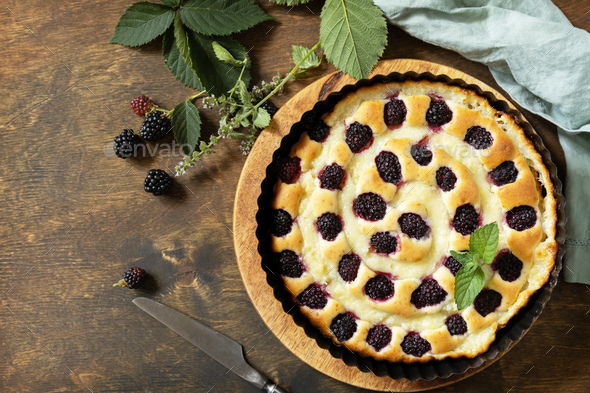 Sweet pie with blackberry and custard on wooden table.