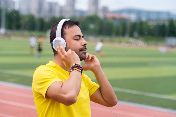 Energized sportsman at city sports stadium listens to his favorite music  through wireless headphones Stock Photo by demopicture