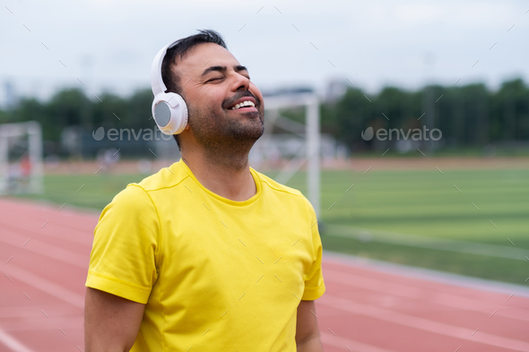 Energized sportsman at city sports stadium listens to his favorite music  through wireless headphones Stock Photo by demopicture