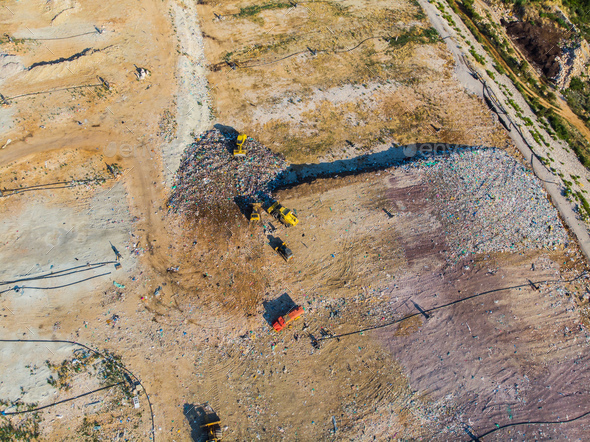 Aerial view from above of dumping site. Garbage trucks. Yellow tractor. Waste sorting. Landfill of