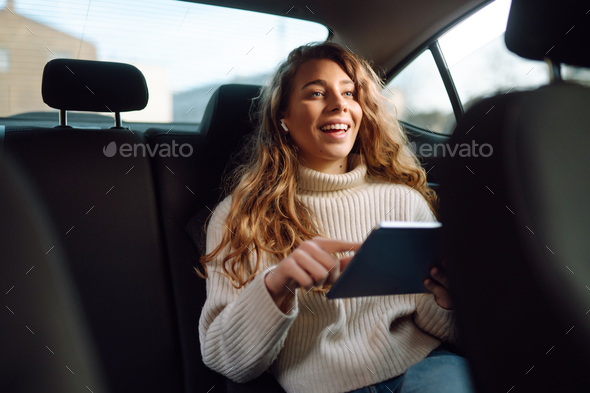 Woman sitting in back seat of car with tablet in hand. Business, taxi, technologie, online concert.