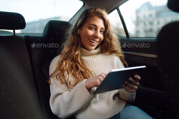 Woman sitting in back seat of car with tablet in hand. Business, taxi, technologie, online concert.
