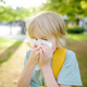 Preteen boy sneezing and wipes nose with napkin during walking in summer park.  - PhotoDune Item for Sale