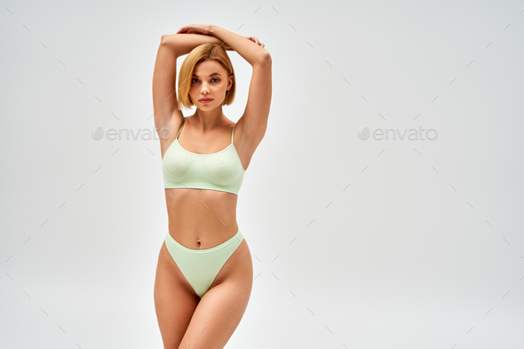Confident and pretty young blonde woman in light green panties and bra  posing Stock Photo by LightFieldStudios