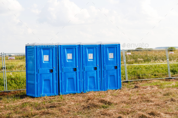 four blue of portable bio toilet cabins in field. Line of chemical toilets for the holiday, festival