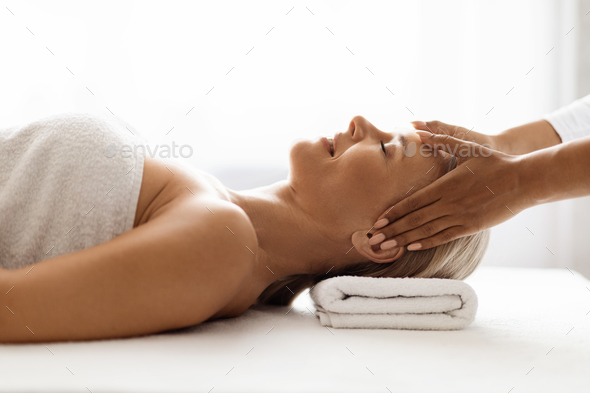 Masseur making acupressure face massage for attractive middle aged woman at spa
