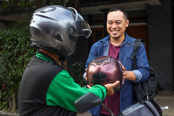 motorbike taxi driver giving helmet to passenger