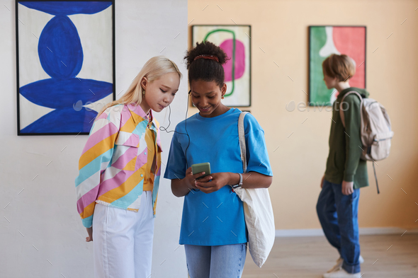 Two teenage girls listening to online guide in art gallery