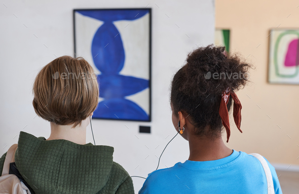 Back view two teenagers in art gallery sharing earphones with audio guide
