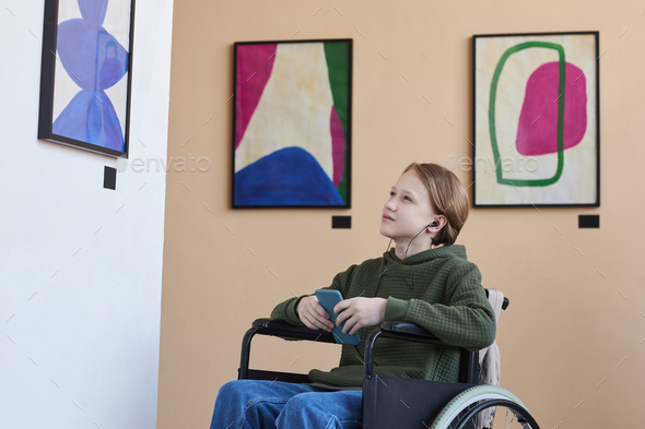 Teenage boy with disability in art gallery and listening to audio guide