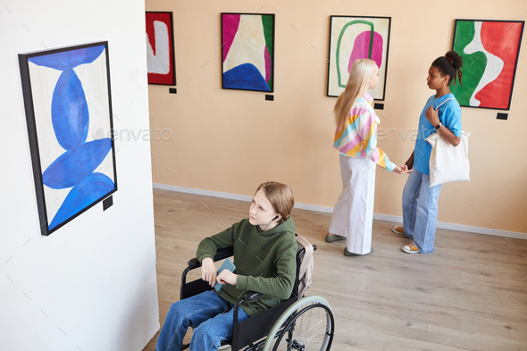 Boy with disability looking at abstract pictures in art gallery