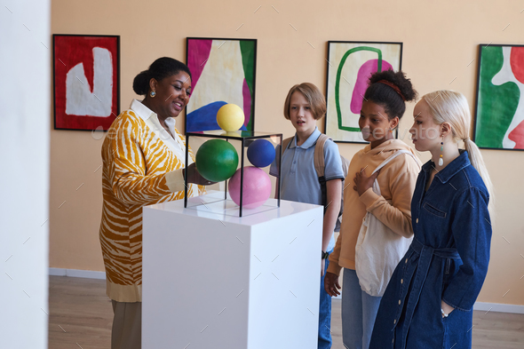 Teenagers listening to teacher or tour guide in modern art gallery