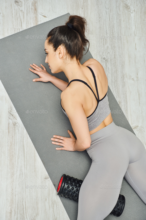 Top view of young brunette woman in sportswear massaging leg with