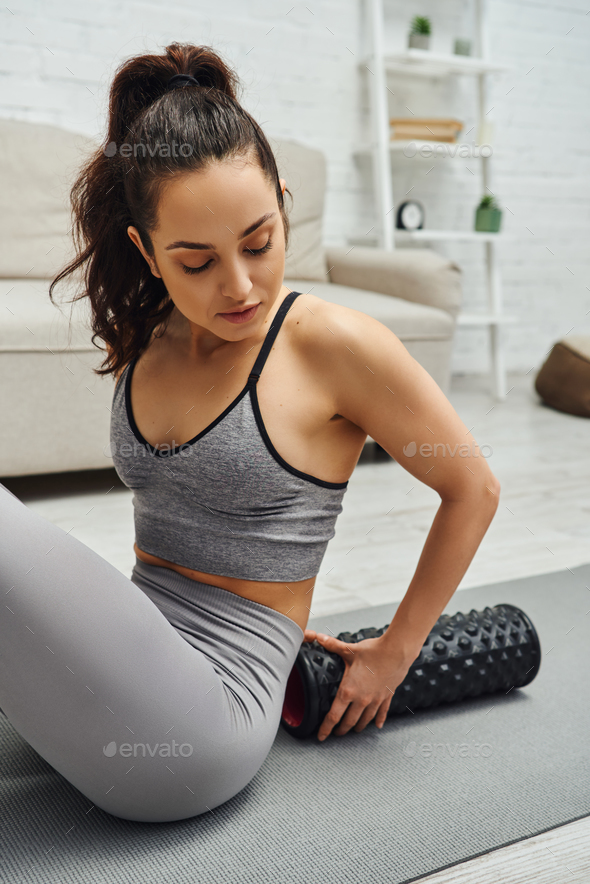 Young brunette woman in activewear holding modern roller massager for lymphatic  drainage Stock Photo by LightFieldStudios