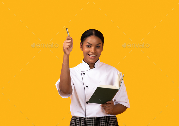 Cooking Idea. Excited Black Chef Woman Holding Cookbook And Pen