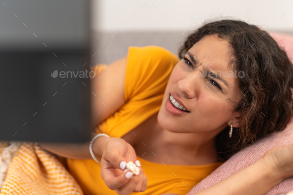 Young woman lying down eating popcorn and watching a series