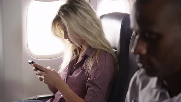 Young woman using mobile phone on airplane flight