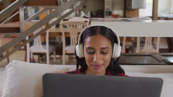 Mixed race woman on couch at home using laptop listening to music alt