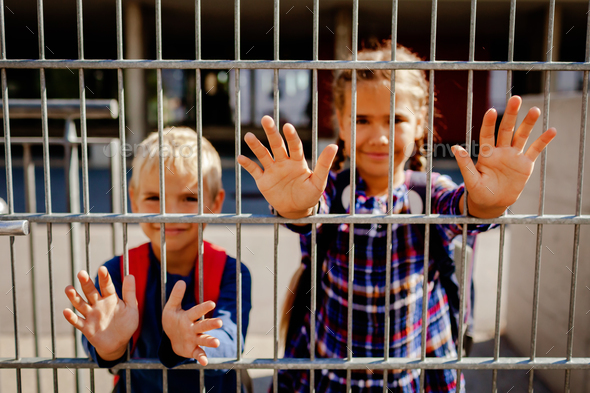 Primary school kids put hands through the gate to wave to their parents. Back to school. Education