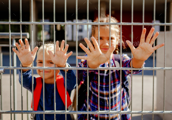 Primary school kids put hands through the gate to wave to their parents. Back to school. Education