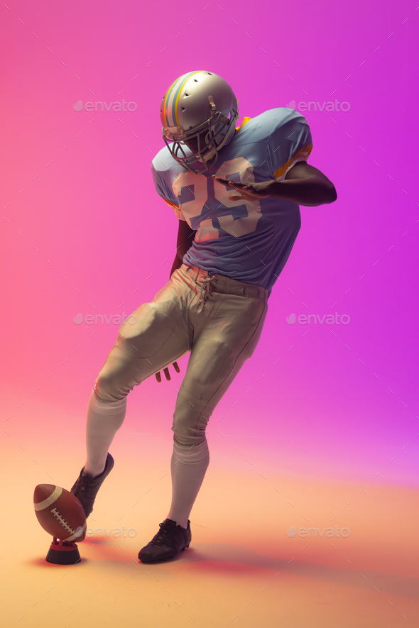 African american male american football player kicking ball with neon pink lighting
