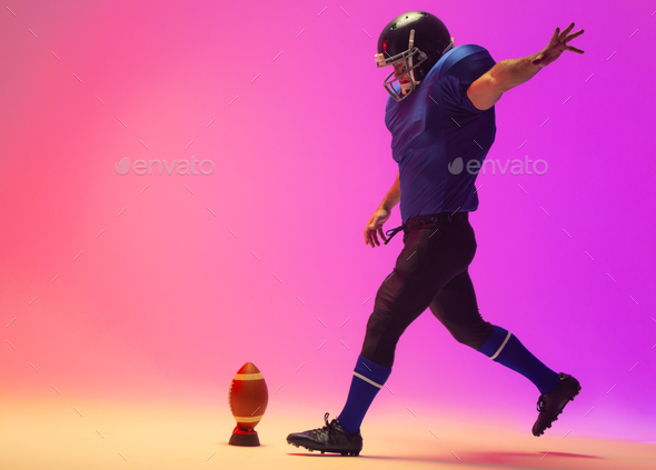 Caucasian male american football player kicking ball with neon pink lighting