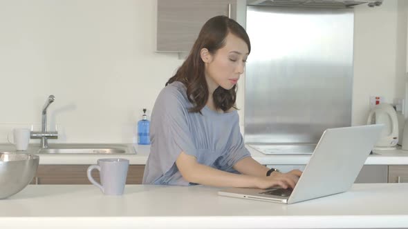 MS Young woman drinking coffee and working on laptop in kitchen