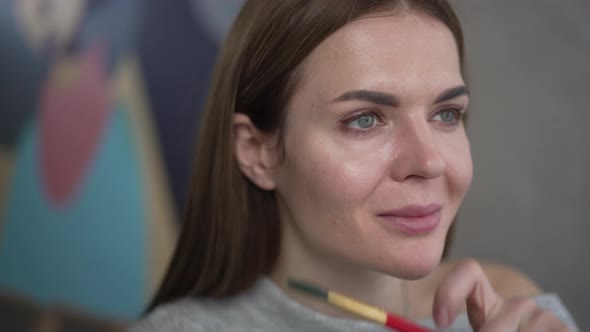 Headshot Portrait of Beautiful Female Artist Looking Away Smiling Sitting with Painting Brush alt
