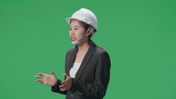 Side View Of Smiling Asian Female Engineer Holding Her Hands And Talking In The Green Screen Studio alt
