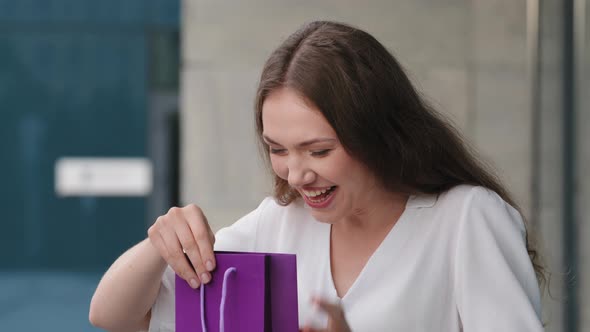 Young Caucasian Girl Woman Exited Lady Receiving Purple Package Gift Bag From Unknown Person Looking alt