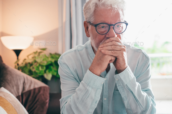 Sad depressed senior man sitting at home alone staring into space, old bearded man with problems