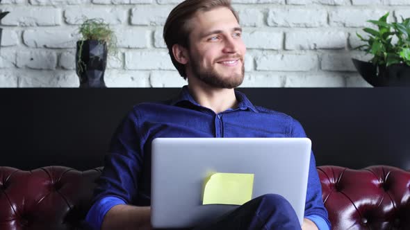 Smiling young businessman using laptop notebook working on table at home, happy man surfing web look alt