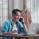 Asian Male Designer With Sewing Machine Talking On Smartphone While Designing Clothes On Laptop - VideoHive Item for Sale