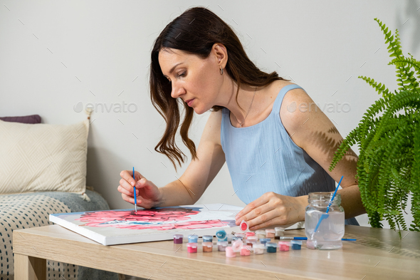 Painting by numbers. Woman drawing picture by numbers with acrylic paints on canvas at home.