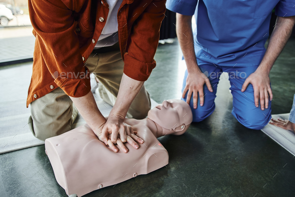 partial view of young man doing chest compressions on CPR manikin during first aid seminar