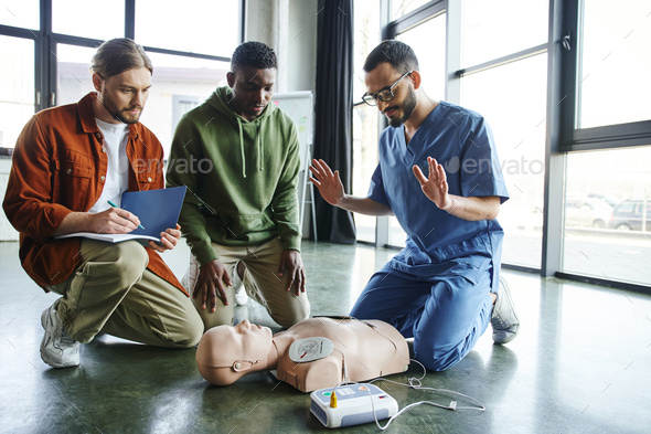 young paramedic explaining cardiac resuscitation techniques to interracial participants near CPR