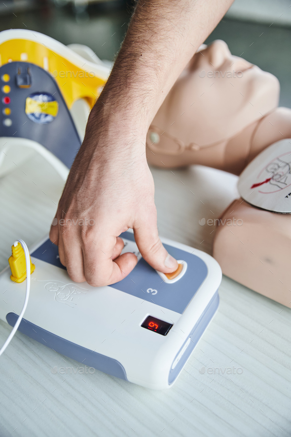 partial view of healthcare worker operating automated defibrillator while practicing cardiac